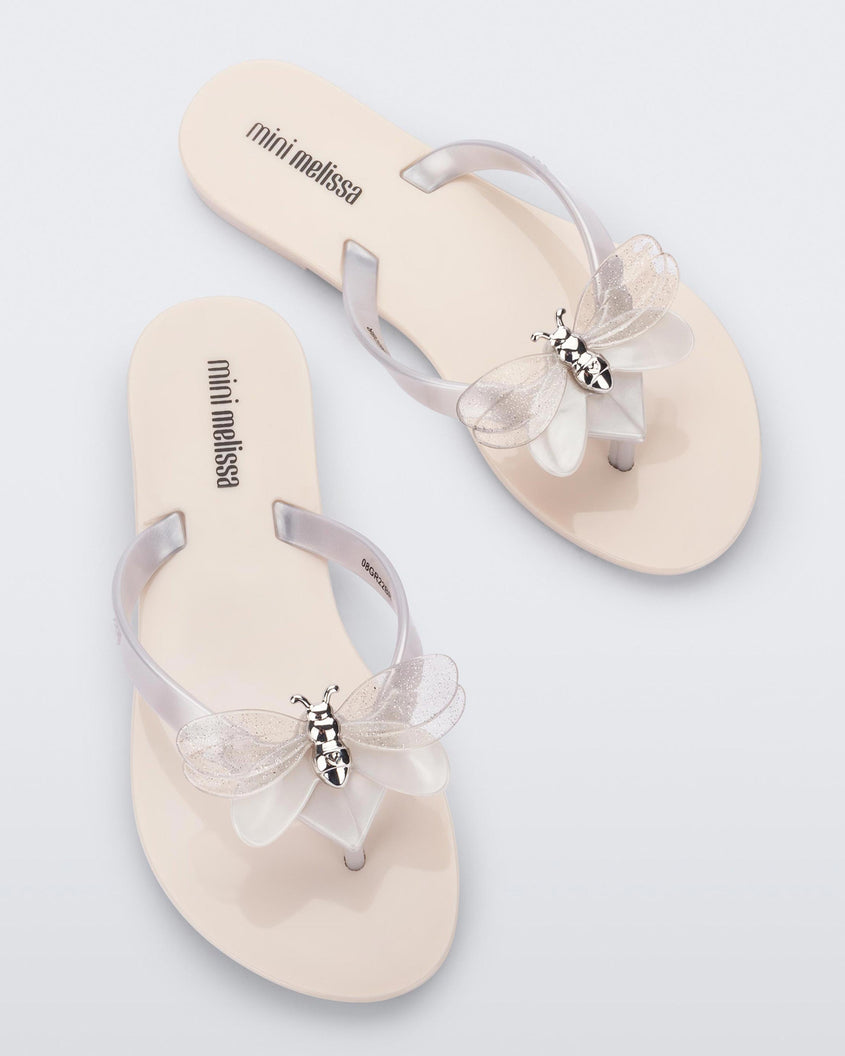 Top view of a pair of beige / metallic white Mini Melissa's Harmonic Bugs flip flop with a clear glitter bug with a silver buckle on the straps.