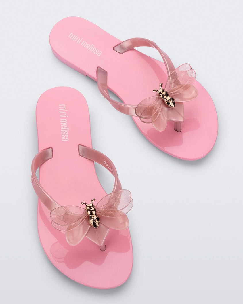 A top view of a pair of pink / pearly pink Mini Melissa Harmonic Bugs flip flops with a clear glitter bug with a gold buckle on the straps.