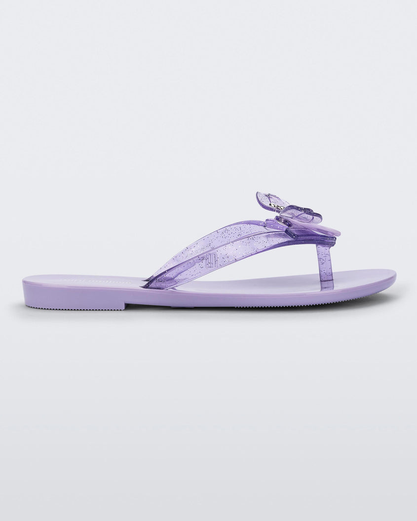 Side view of a lilac / lilac glitter Mini Melissa Harmonic Bugs flip flop with a clear glitter bug with a silver buckle on the straps.