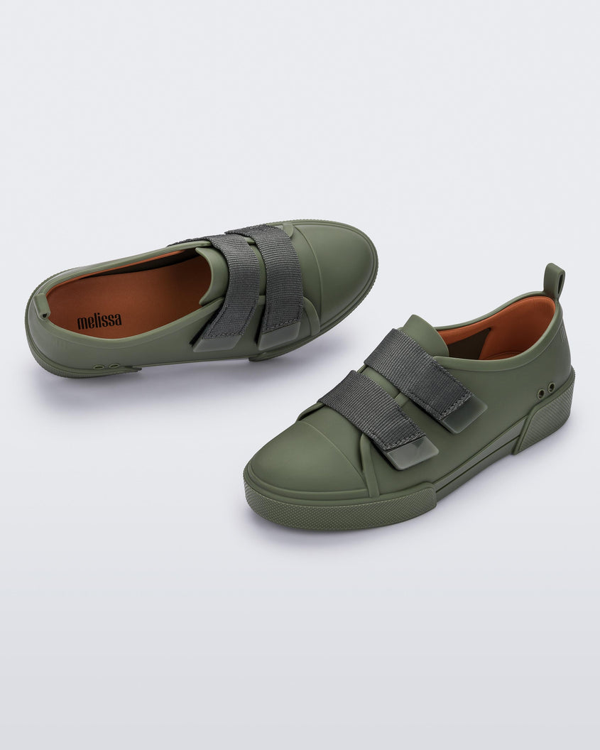 An angled side and top view of a pair of green/orange Melissa Cool sneakers with an orange insole, green base and two green velcro straps.