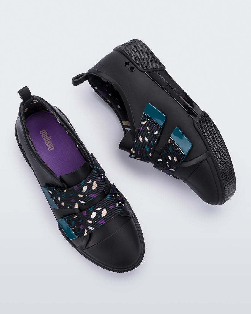 top and side view of a pair of black/purple Melissa Cool sneakers with a purple insole, black base and two black, blue, purple and beige patterned velcro straps.