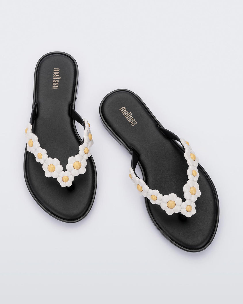A top view of a pair of black Melissa Spring Flip Flops with white and yellow flowers on them.