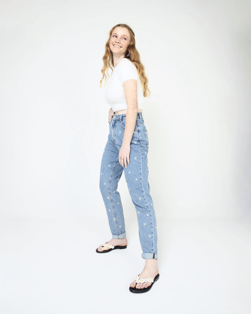 A model posing for a picture wearing a pair of black Melissa Spring Flip Flops with white and yellow flowers on them.