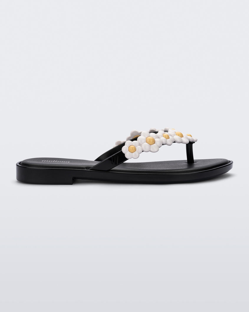 Side view of a black Melissa Spring Flip Flop with white and yellow flowers on them.