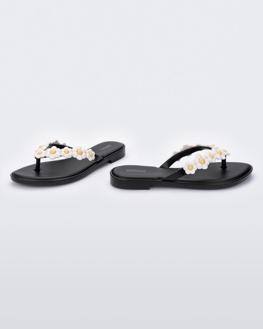 A side and front view of a pair of black Melissa Spring Flip Flops with yellow and white flowers on them.