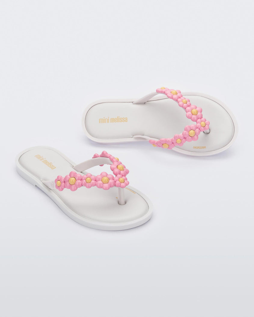 A top and side view of a pair of white Mini Melissa Spring Flip Flops with yellow and pink flowers.