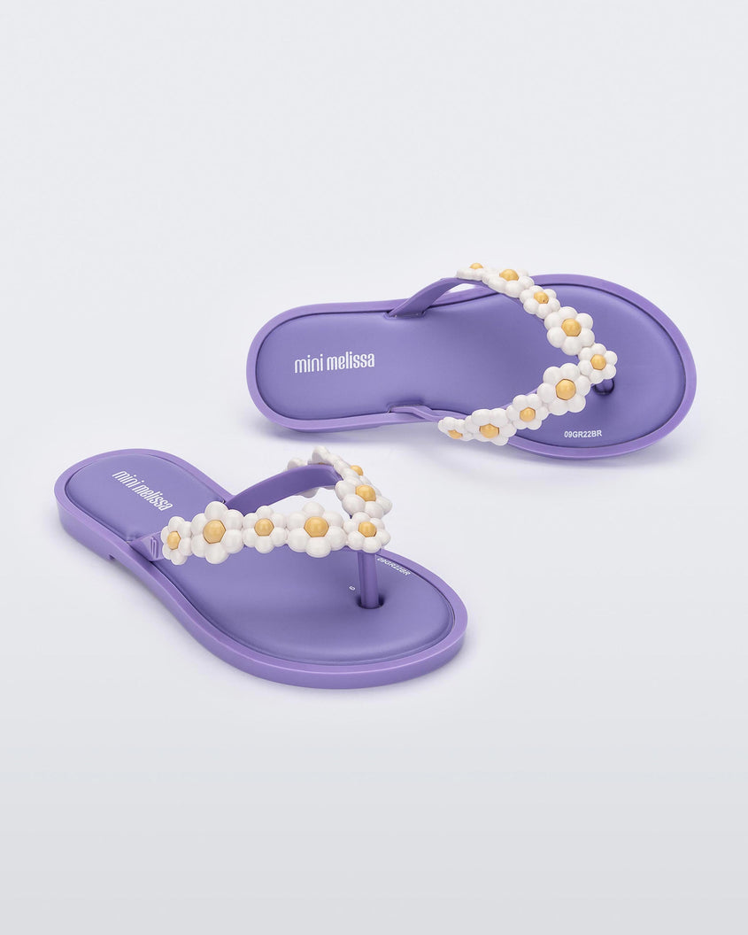 A top and side view of a pair of lilac Mini Melissa Spring Flip Flops with yellow and white flowers.
