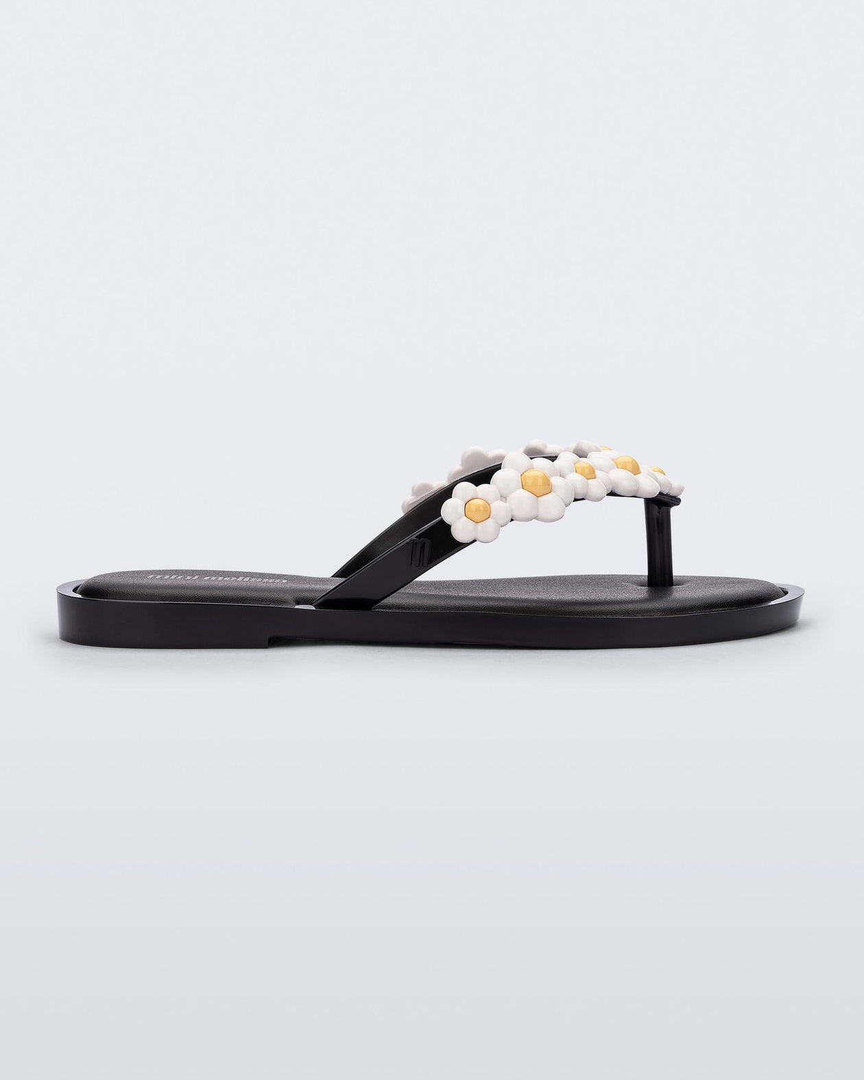 Side view of a black Mini Melissa Spring Flip Flop with white and yellow flowers.