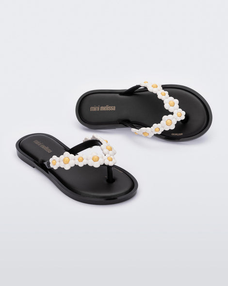 A top and side view of a pair of black Mini Melissa Spring Flip Flops with yellow and white flowers.