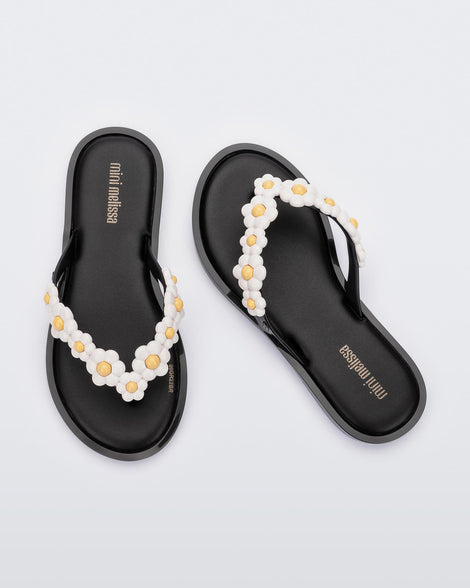 A top view of a pair of black Mini Melissa Spring Flip Flops with yellow and white flowers.