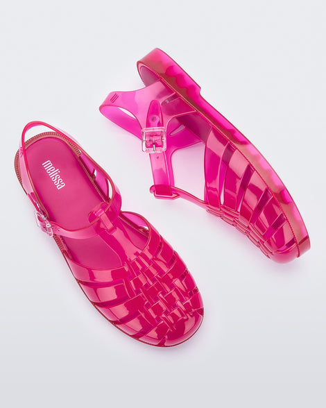 Top and side view of a pair of transparent pink Melissa Possession sandal with a closed toe front weft design connected to a top strap with a buckle.
