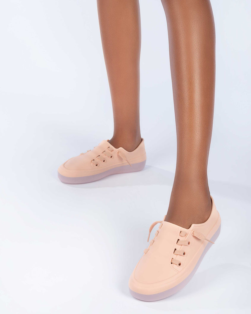 A model's legs wearing a pair of pink Melissa Ulitsa sneakers with a pink base and laces.
