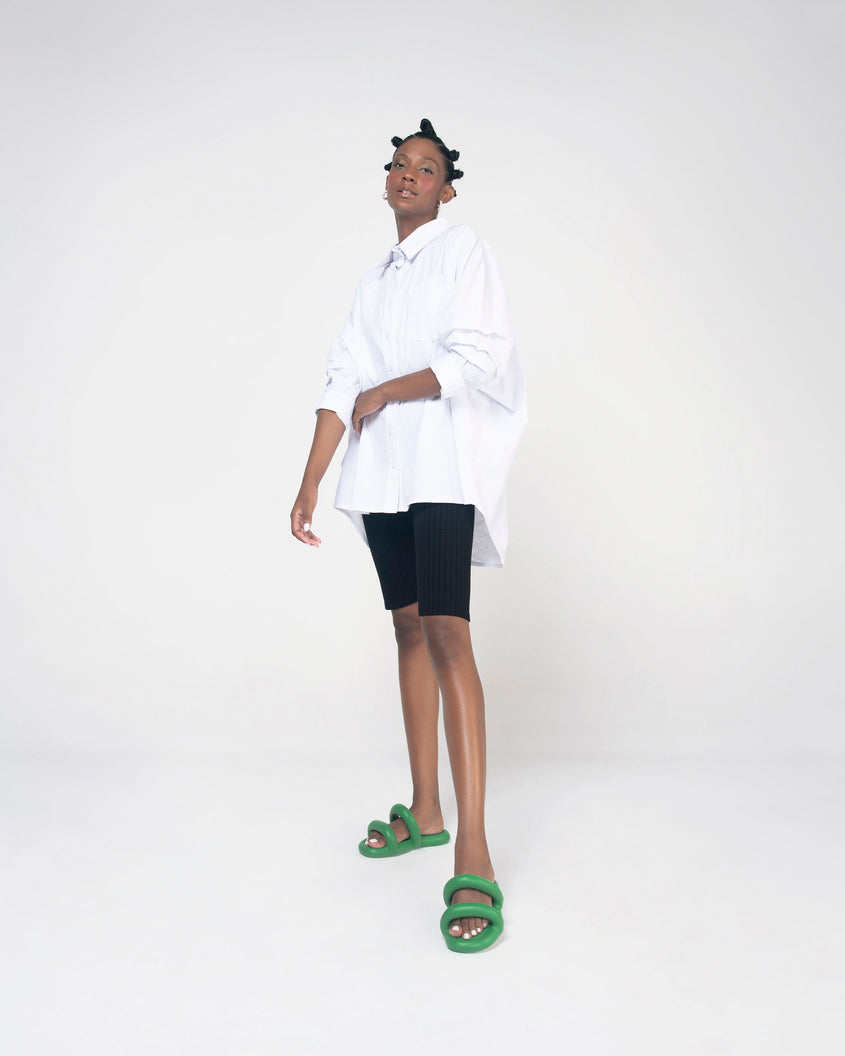 A model in a white shirt and black shorts posing for a picture wearing a pair of green Melissa Free Bloom Slides with puffer-like straps.