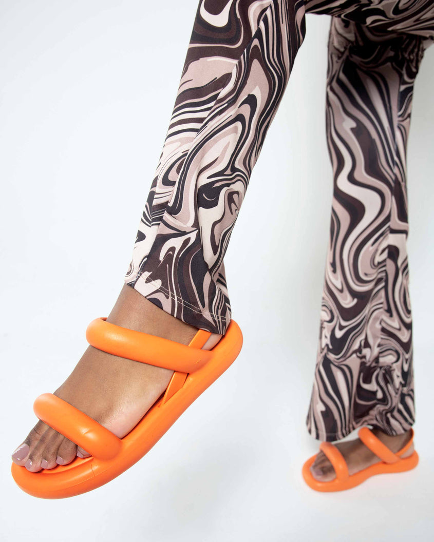 A model's legs in patterned pants wearing a pair of orange Melissa Free Bloom Sandals with puffer-like straps.