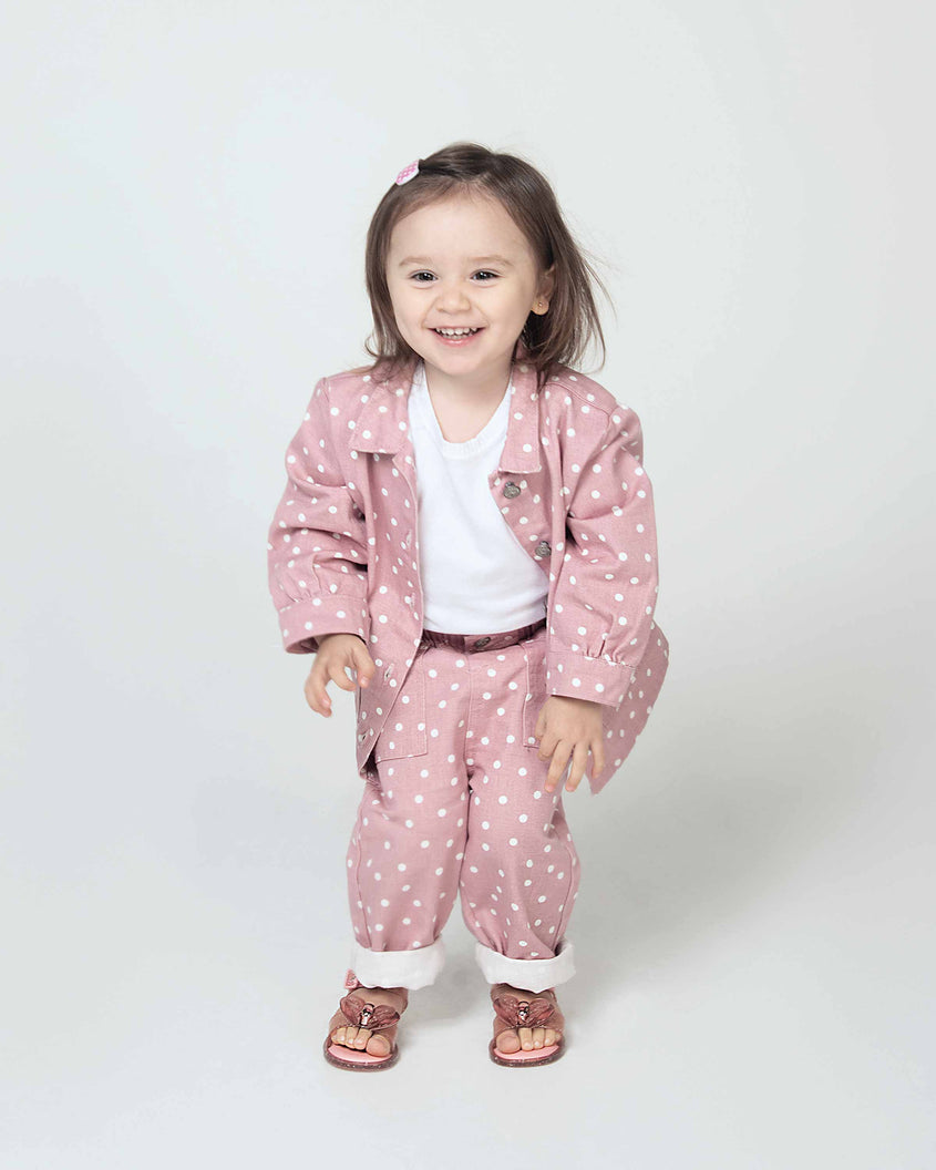 A model in a pink polka dot top and bottom wearing a pair of pink glitter Mini Melissa Mar Sandals with a pink heart shaped bow and buckle.