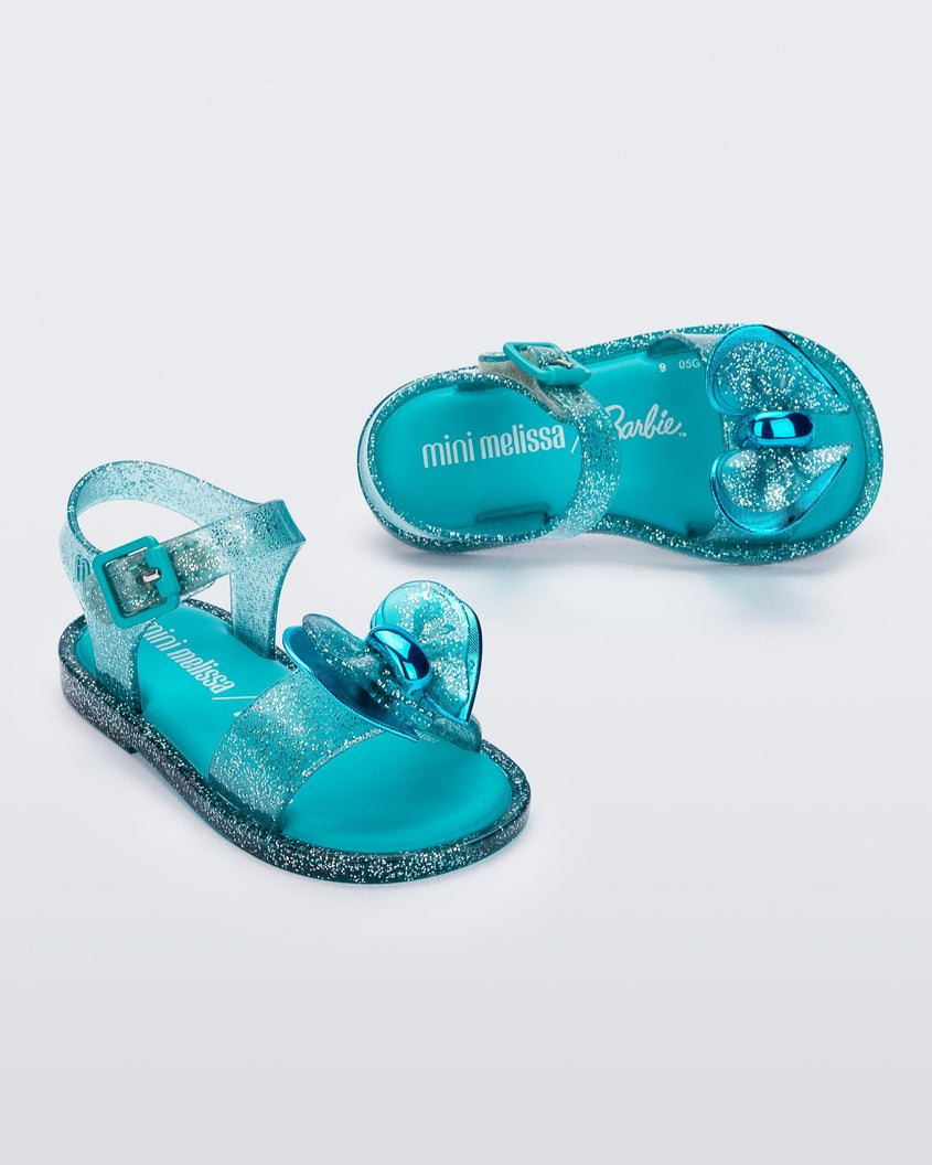 Top and side view of a pair of blue glitter Mini Melissa Mar sandals with a bow.