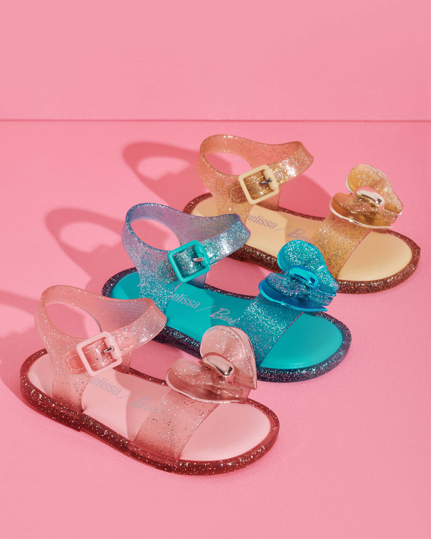 A group 3 pairs of Mini Melissa Mar Sandals with bows in glitter pink, glitter blue, and glitter gold.