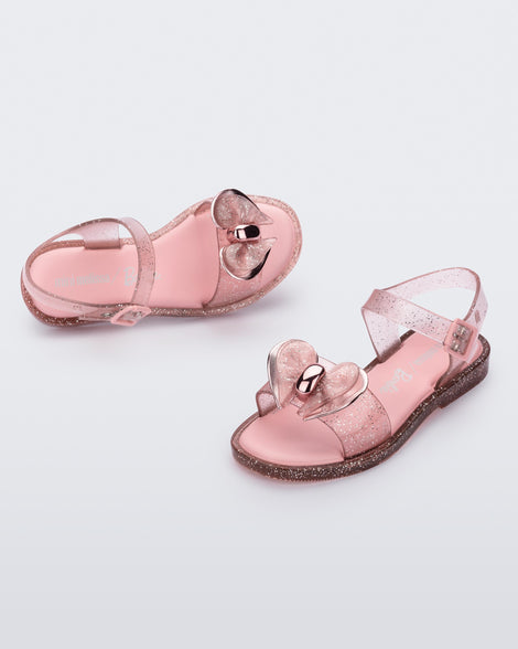 Angled view of a pair of glitter pick Mini Melissa Mar Sandals with a bow.