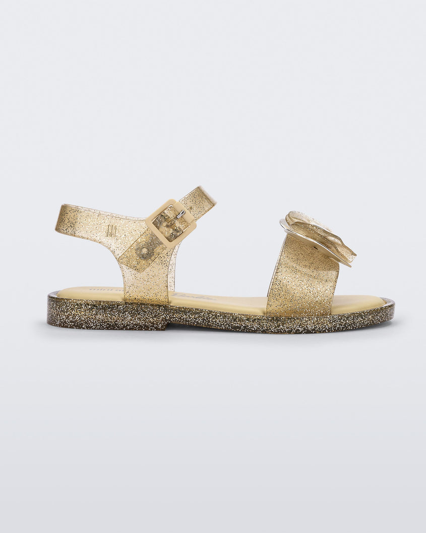 Side view of a gold glitter Mini Melissa Mar sandal with a bow.