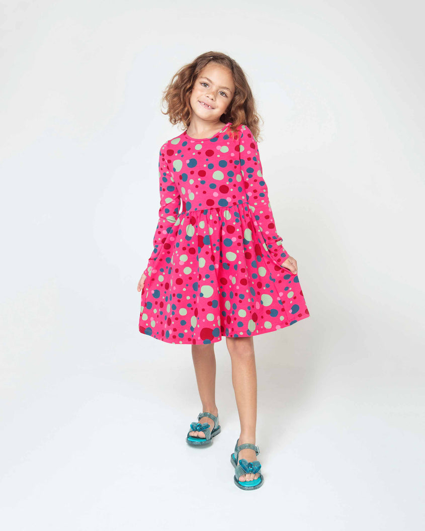 A little girl wearing a pink dress and a pair of blue Mini Melissa Mar Sandals.
