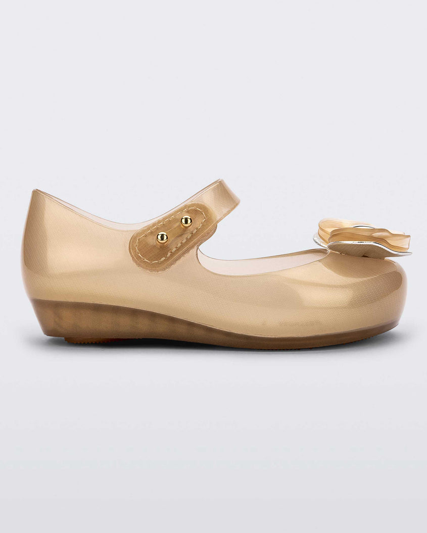 Side view of a pearly biege Mini Melissa Ultragirl flat with a top strap and a heart shaped bow buckle on the toe.