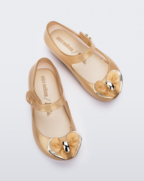 Top view of a pair of pearly biege Mini Melissa Ultragirl flats with a top strap and a heart shaped bow buckle on the toe.