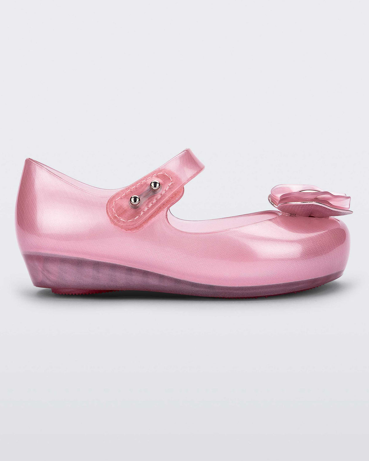 Side view of a pearly pink Mini Melissa Ultragirl flat with a top strap and a heart bow buckle detail on the toe.