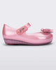 Side view of a pearly pink Mini Melissa Ultragirl flat with a top strap and a heart bow buckle detail on the toe.