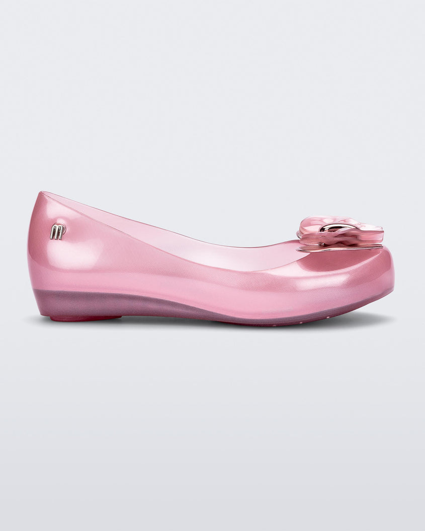 Side view of a pearly pink Mini Melissa Ultragirl flat with a heart buckle bow detail on the toe.