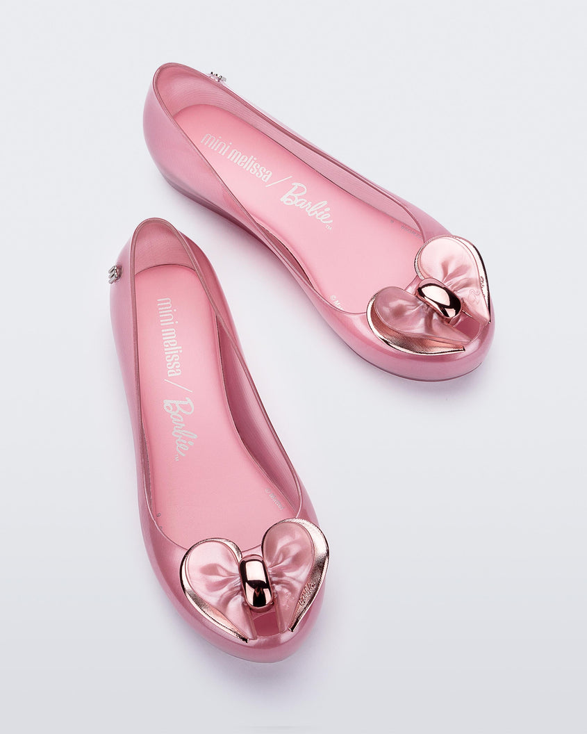 Top view of a pair of pearly pink Mini Melissa Ultragirl flats with a heart buckle bow detail on the toe.