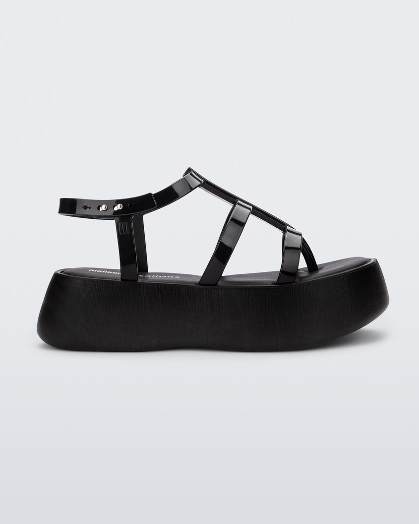 Side view of a black Melissa Caribe High Platform sandal with two black front straps joined by a vertical strap intersecting the ankle strap and a black sole.