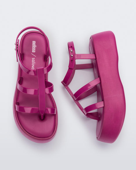 A top and side view of a pair of pink Melissa Caribe High Platform sandals with two pink front straps joined by a vertical strap intersecting the ankle strap and a black sole.