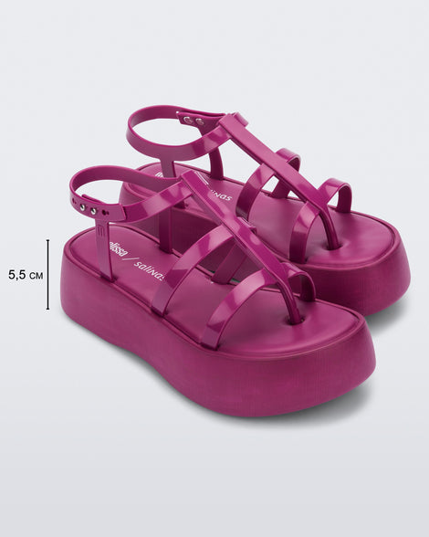 An angled side view of a pair of pink Melissa Caribe High Platform sandals with two pink front straps joined by a vertical strap intersecting the ankle strap and a black sole. The photo also shows the dimensions of the platform which reads 5.5 centermeters.