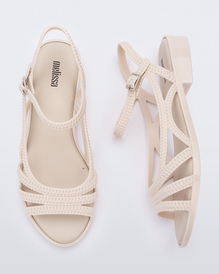 A top and side view of a pair of beige Melissa Femme Classy sandals with straps and a woven design.
