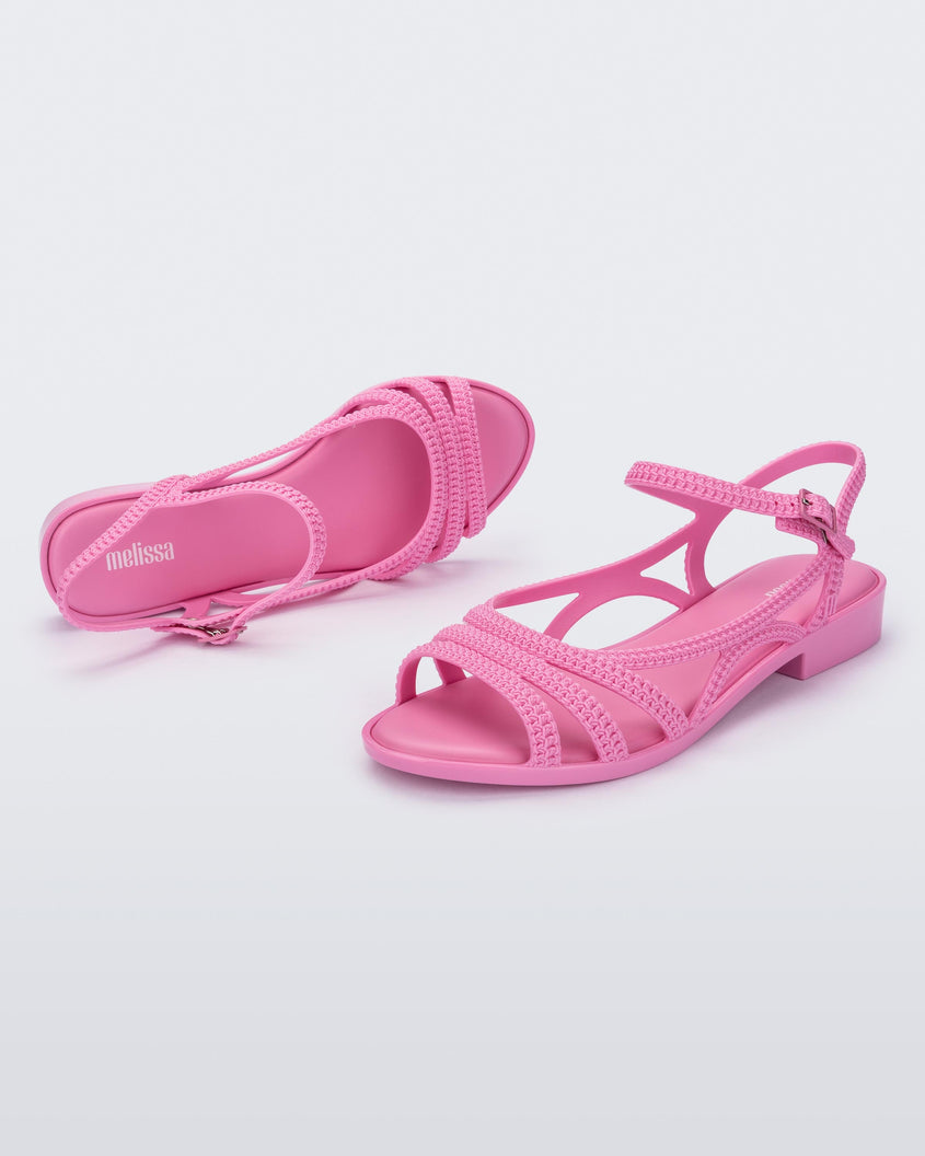 A top and side view of a pair of pink Melissa Femme Classy sandals with straps and a woven design.