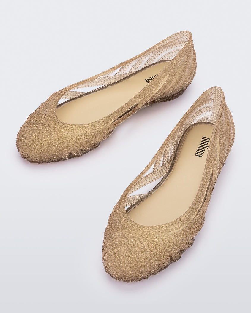 A top view of a pair of beige glitter gold Melissa Femme Classy flats with a woven design.