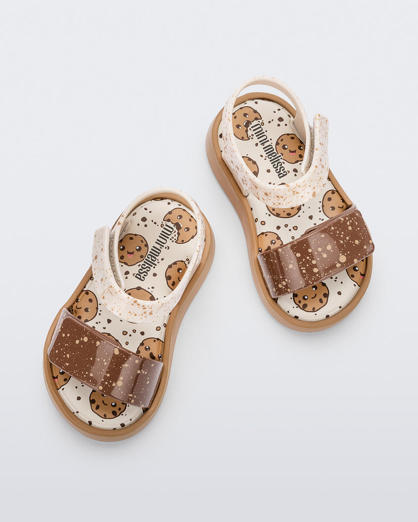 Top view of a beige/brown Mini Melissa Jump Candy sandals with white and brown crumb detail straps and a print of cookies on the insole.