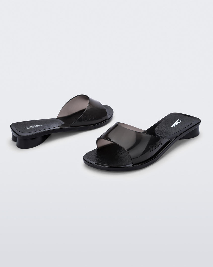 An angled front and side view of a pair of transparent black Melissa Kim slides.