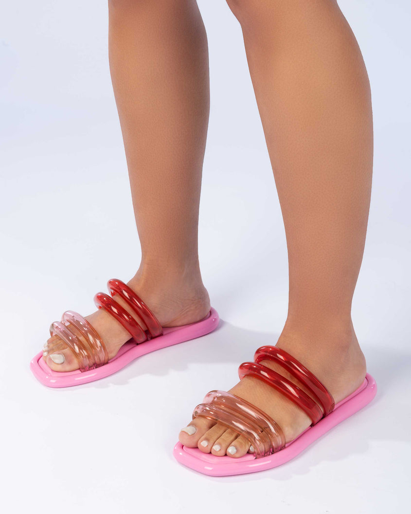 A model's legs wearing a pair of pink and transparent pink Melissa Airbubble slides.