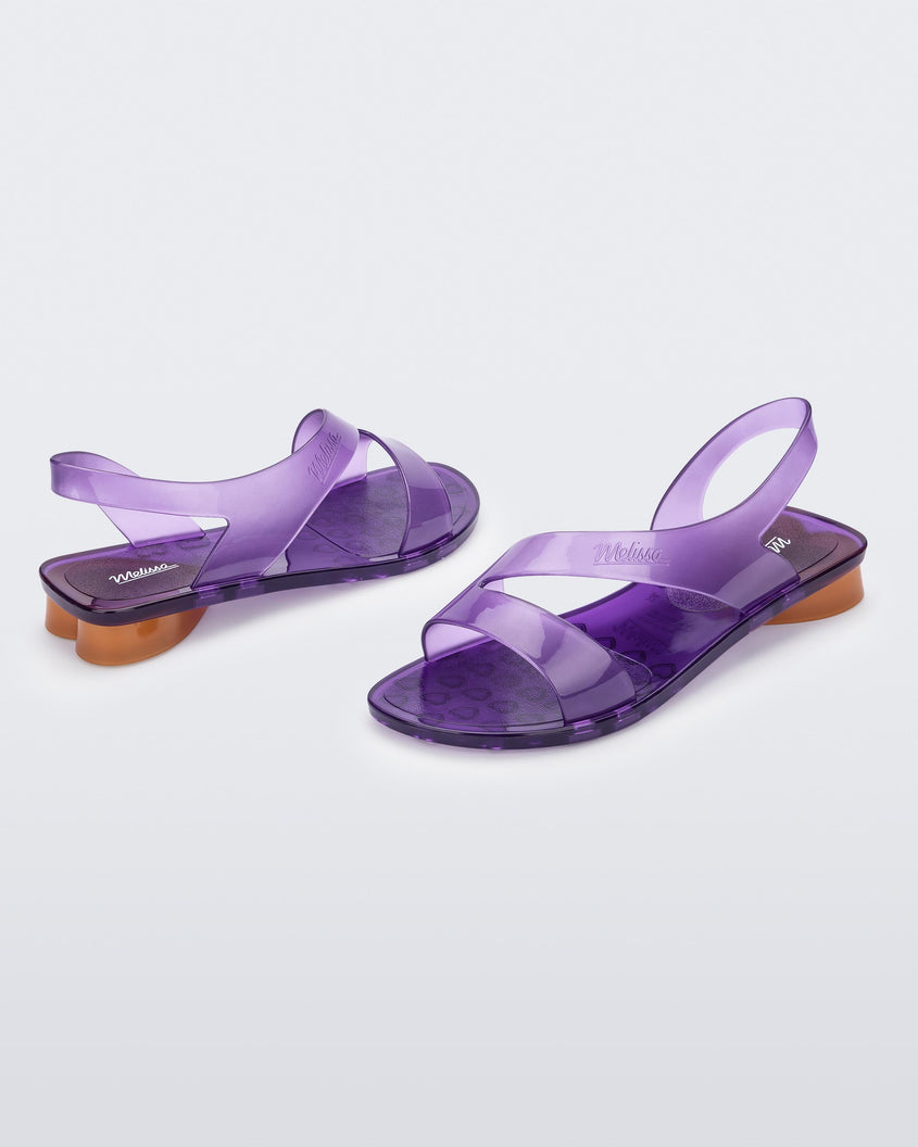An angled front and side view of a pair of purple Melissa The Real Jelly Paris sandals with two front straps, an ankle strap and an orange heel.