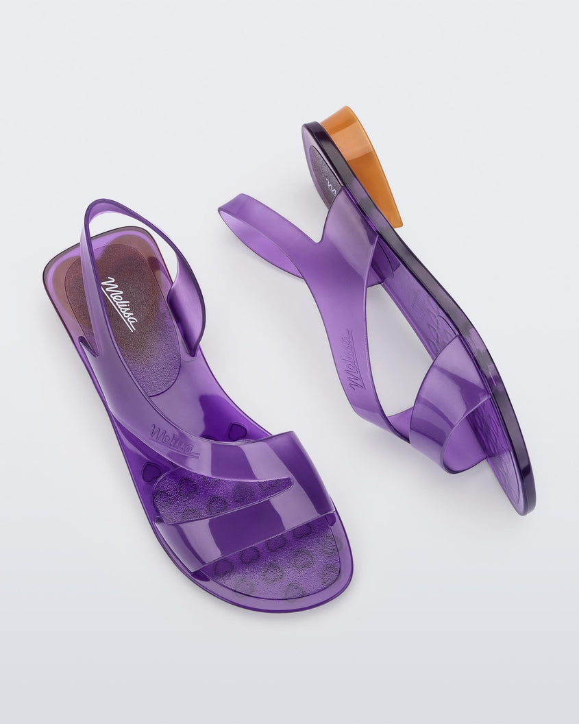 A top and side view of a pair of purple Melissa The Real Jelly Paris sandals with two front straps, an ankle strap and an orange heel.