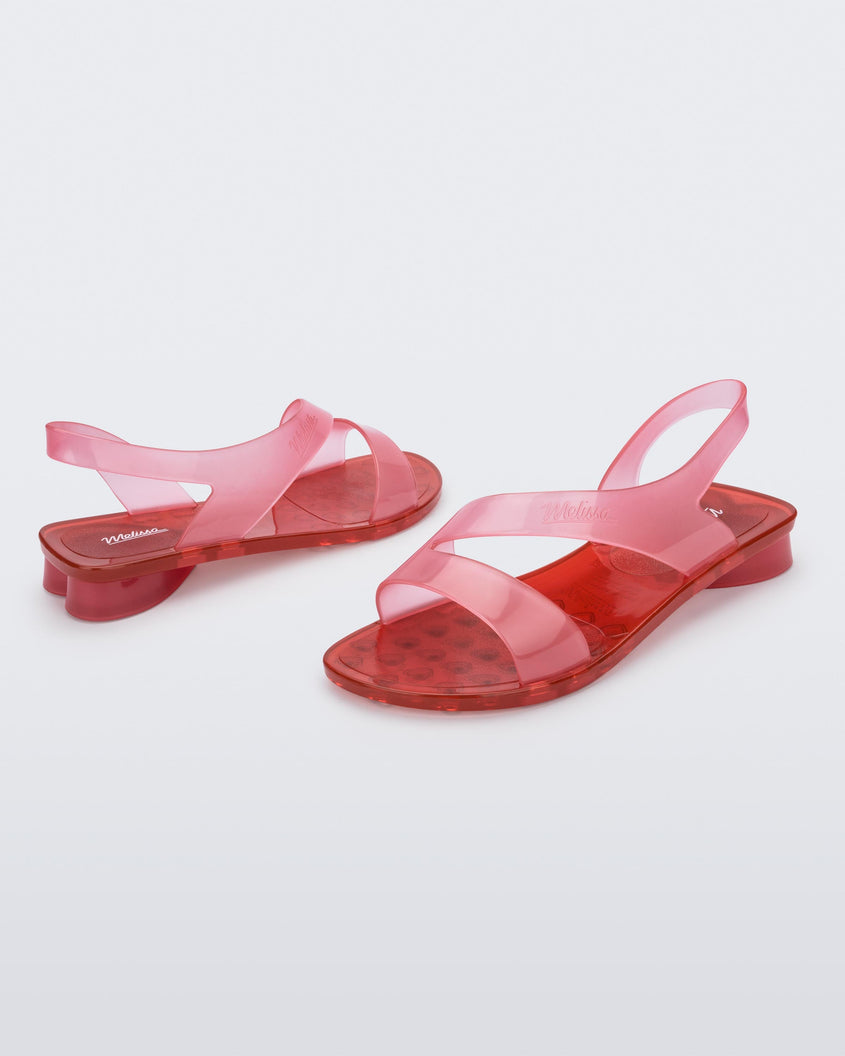 A side view of a pair of pink/red Melissa The Real Jelly Paris sandals with two front straps and an ankle strap.
