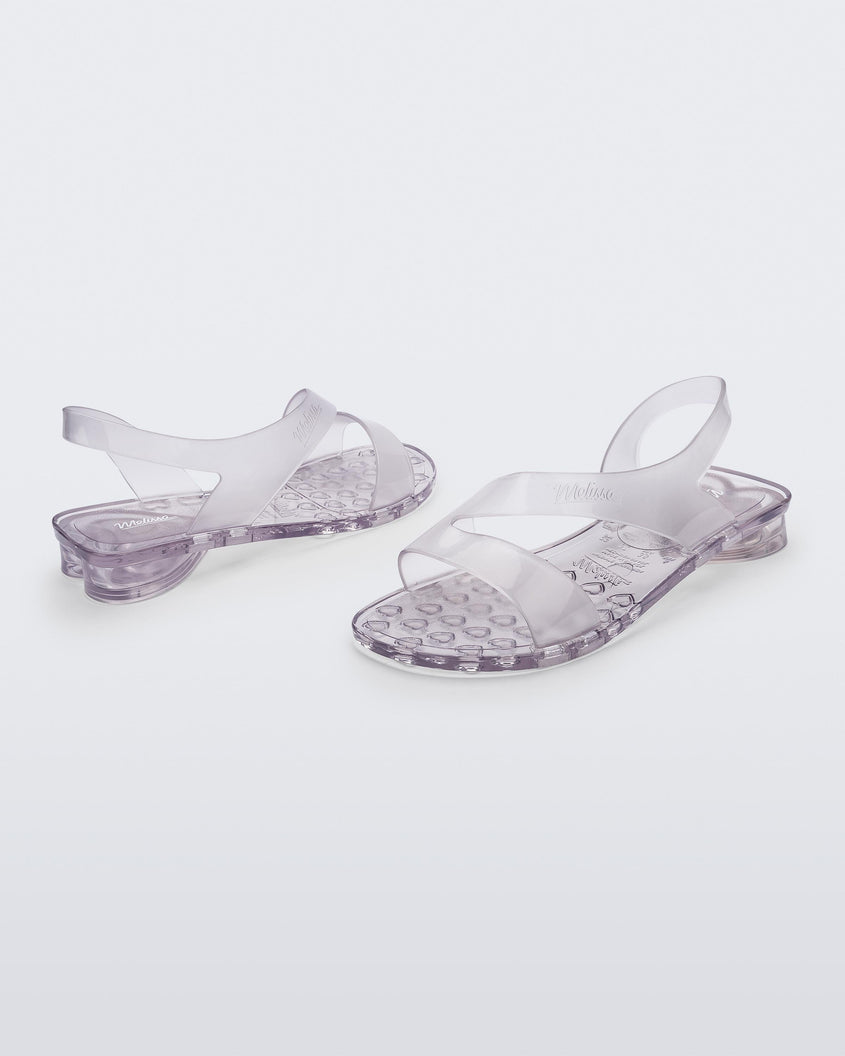 An angled front and side view of a pair of clear Melissa The Real Jelly Paris sandals with two front straps and an ankle strap.