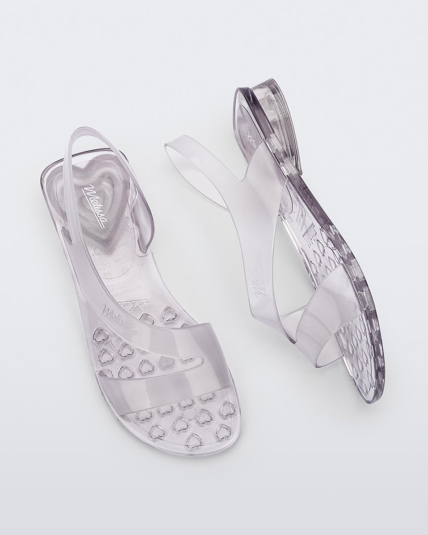 A top and side view of a pair of clear Melissa The Real Jelly Paris sandals with two front straps and an ankle strap.