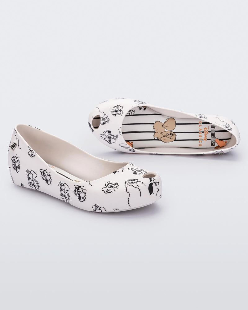 An angled front and side view of a pair of white/grey Mini Melissa Ultragirl Cats & Dogs flats with a white base and cartoon dog face drawing pattern across the base.