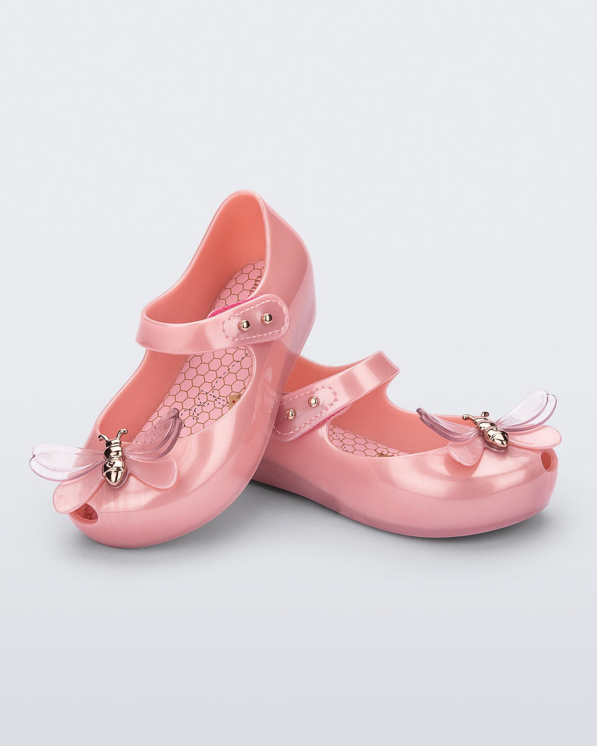 An angled top and side view of a pair of pearly pink Mini Melissa Ultragirl Bugs flats with a top strap and a bug detail on the toe.