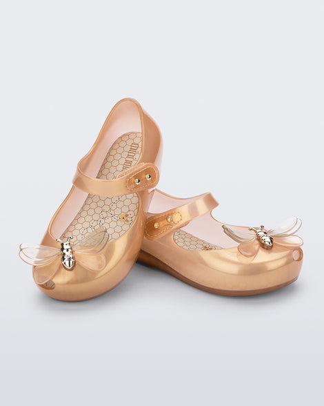 An angled top and side view of a pair of pearly orange Mini Melissa Ultragirl Bugs flats with a top strap and bug detail buckle on the toe.