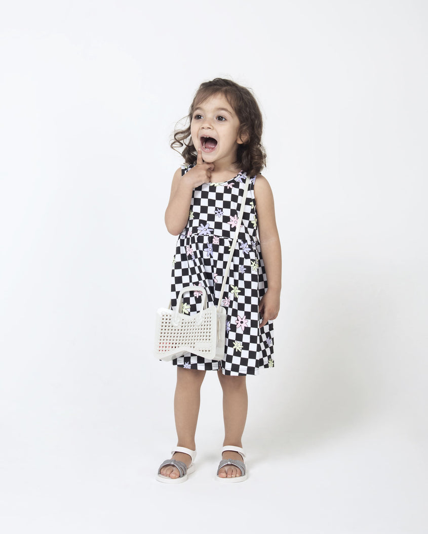 A young model posing for a picture in a black and white dress and a pair of white/silver Mini Melissa Precious sandals with three silver glitter front straps joining in the middle and a white ankle strap.