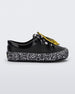 Side view of a black Mini Melissa Street sneaker with an black base, black and white patterned sole, white and black patterned laces with a drawing of bananas on top the laces.