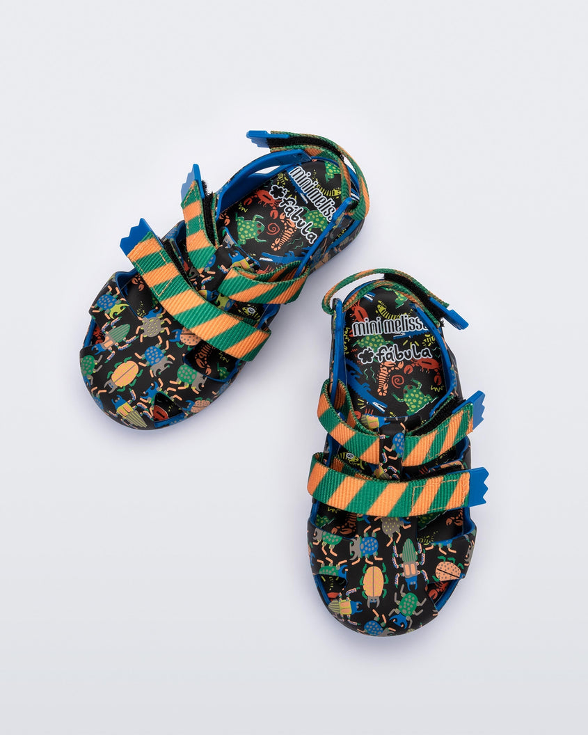 Top view of a pair of blue/green Mini Melissa Yoyo sandals with a black, green and blue patterned base, with two green and orange velcro front straps and an ankle strap.